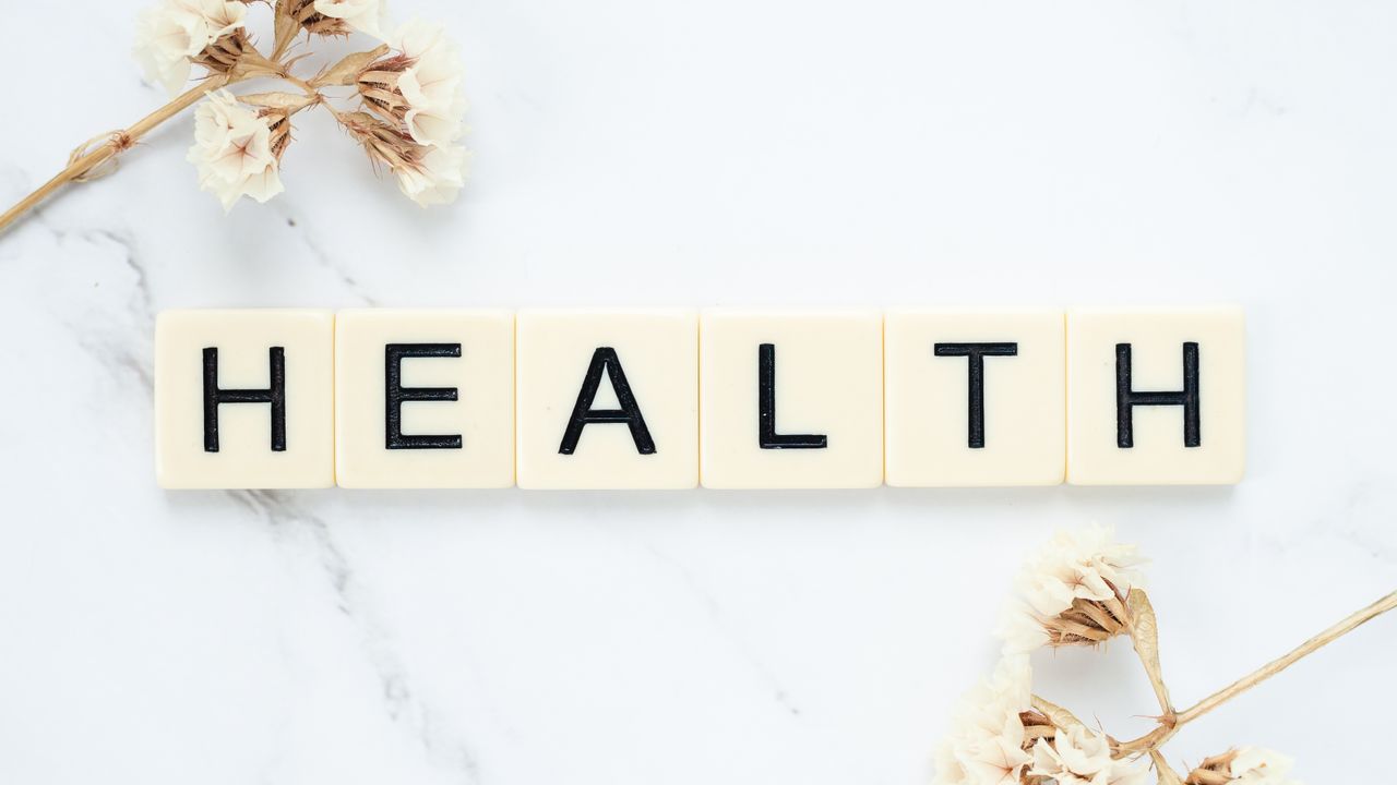 Services Creative arrangement of scrabble tiles spelling Health with white flowers on a marble surface.